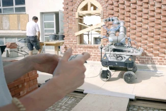 Roboter vor der klimaoptimierten Wand. Links daneben ist ein Handwerker zu sehen.