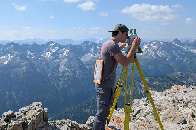 Lukas Raffl schaut durch ein geodätisches Messgerät oben am Berg