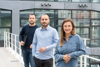 Portrait von drei Menschen vor einem Gebäude.