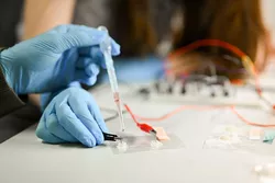 One hand holds a pipette on two electrodes 