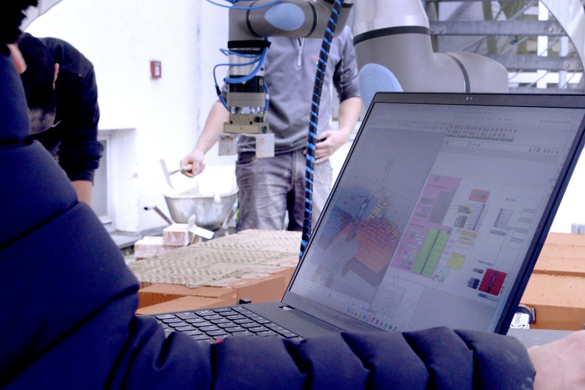 Auf dem Laptop wird eine Simulation erstellt, im Hintergrund ist der Roboter zu sehen.